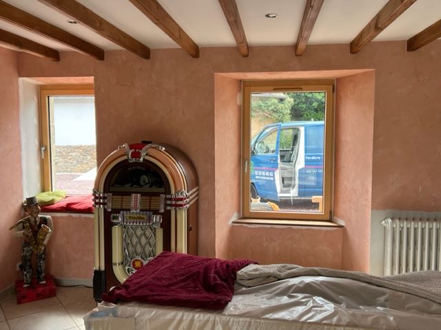 Une chambre avec jukebox, lit et fenêtres donnant sur une camionnette garée. Murs roses et poutres en bois.