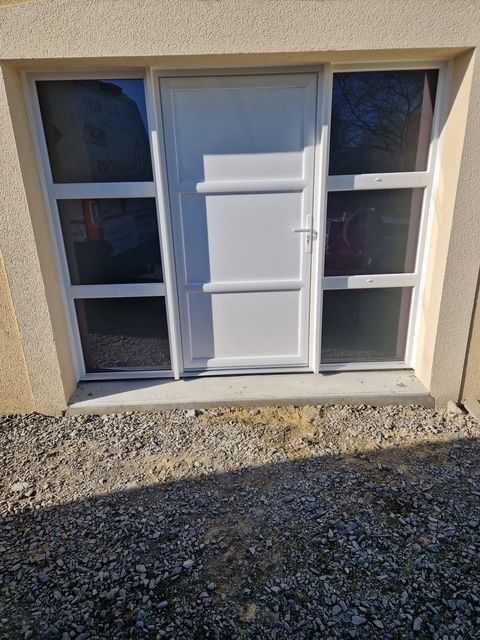 Porte blanche avec fenêtres latérales dans un bâtiment en pierre. Chemin de gravier devant.