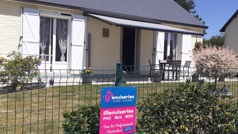 Gîte avec volets blancs et auvent, panneau rose devant.