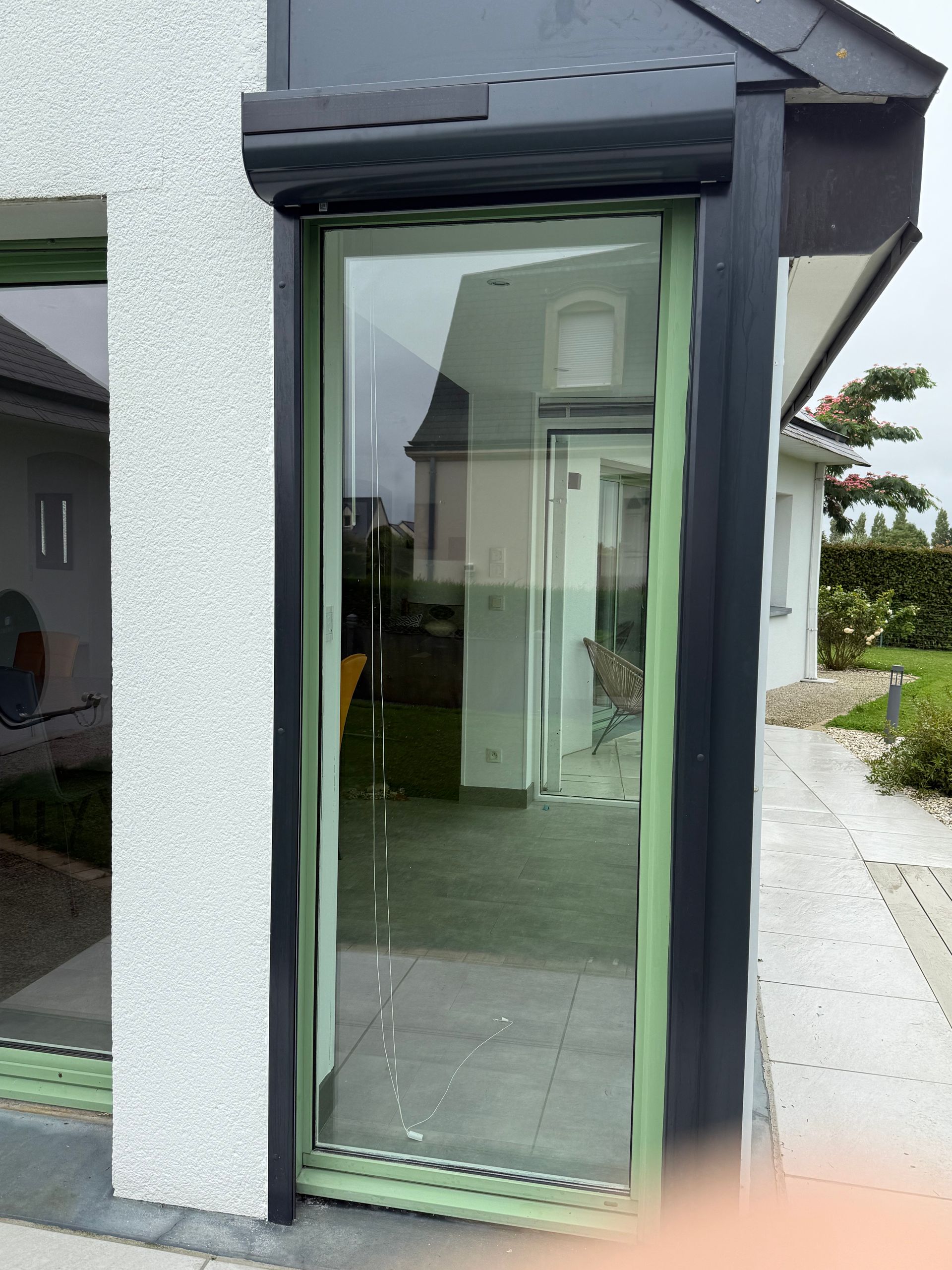 Porte vitrée avec cadre vert et volet roulant foncé sur une maison moderne.