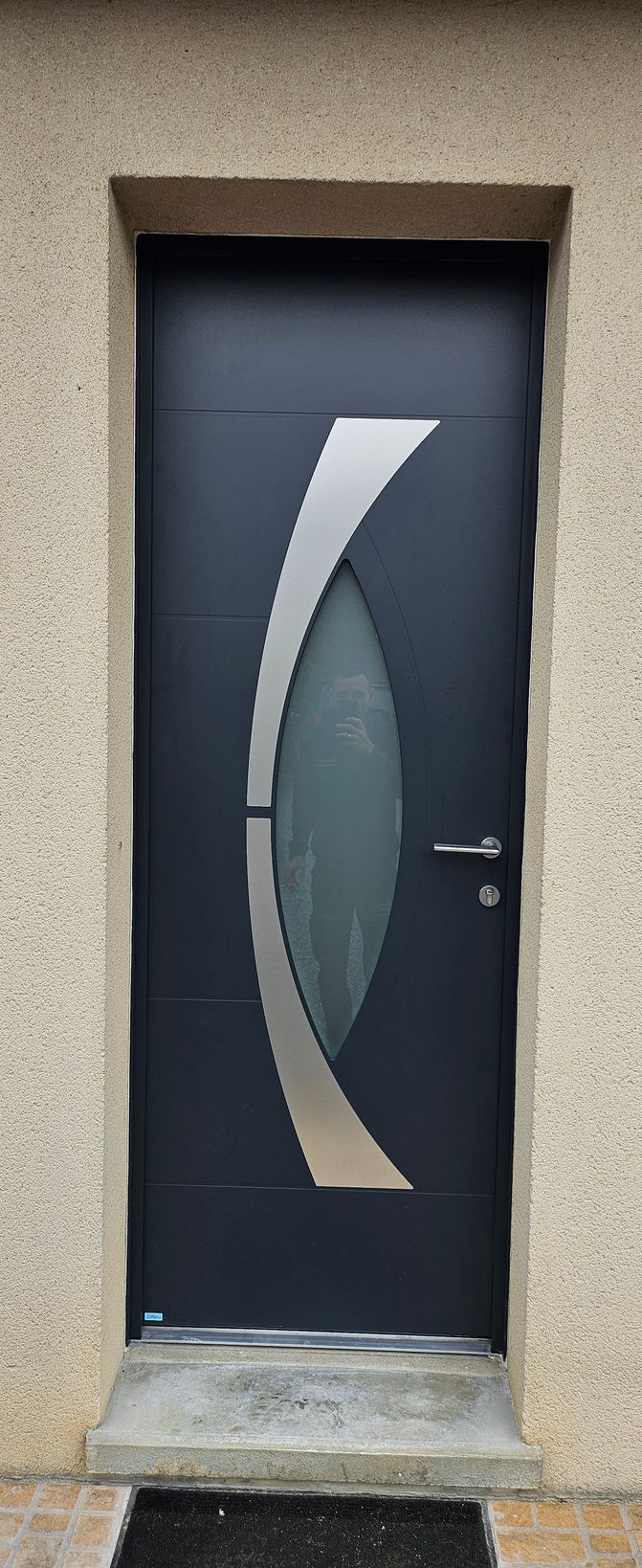 Porte d'entrée noire avec garniture argentée et panneau de verre dans un extérieur beige.