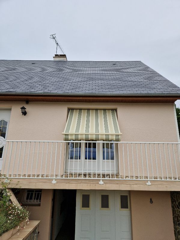 Maison beige avec balcon et auvent, toiture grise, portes de garage blanches.