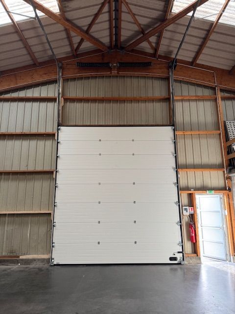 Grande porte industrielle blanche dans un entrepôt, avec une petite porte sur le côté.