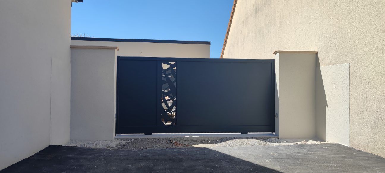 Portail noir avec découpe décorative dans l'entrée d'un bâtiment de couleur claire, ciel bleu.