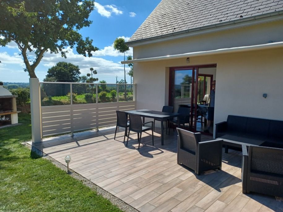 Patio avec mobilier d'extérieur, donnant sur des champs verts et un ciel bleu.