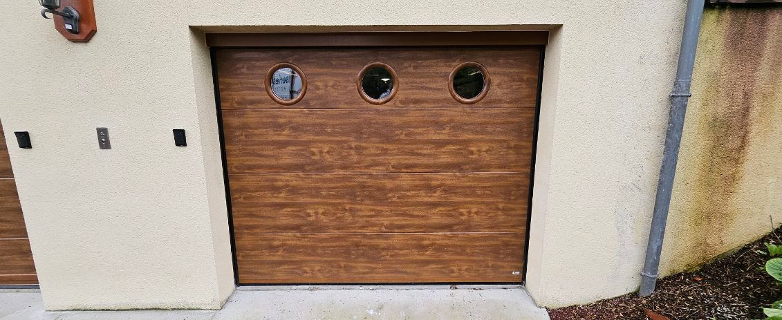 Porte de garage en bois avec trois fenêtres rondes et garniture en stuc beige.
