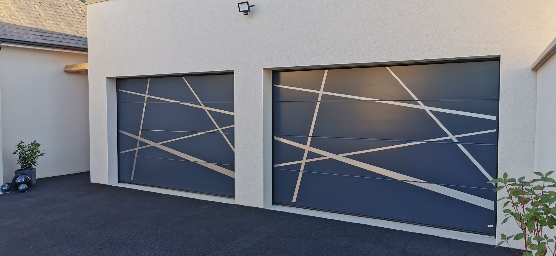 Deux portes de garage bleu foncé avec des lignes géométriques blanches sur un bâtiment blanc.