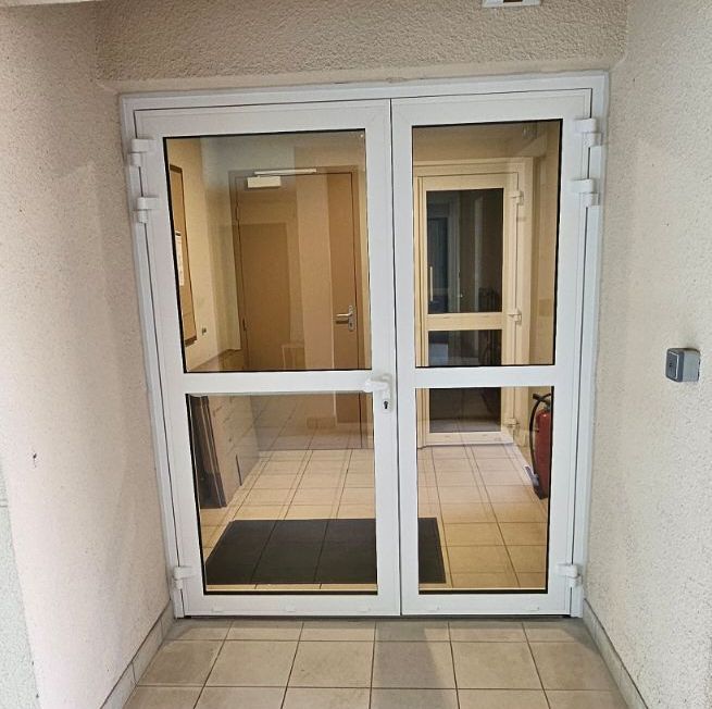 Portes doubles vitrées blanches avec un couloir visible au-delà.