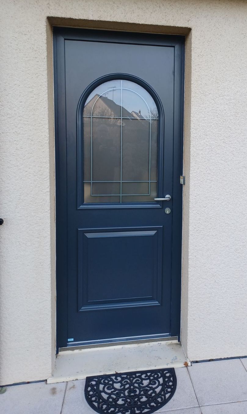 Porte d'entrée bleu foncé avec panneau de verre arqué, encastrée dans un mur beige clair.
