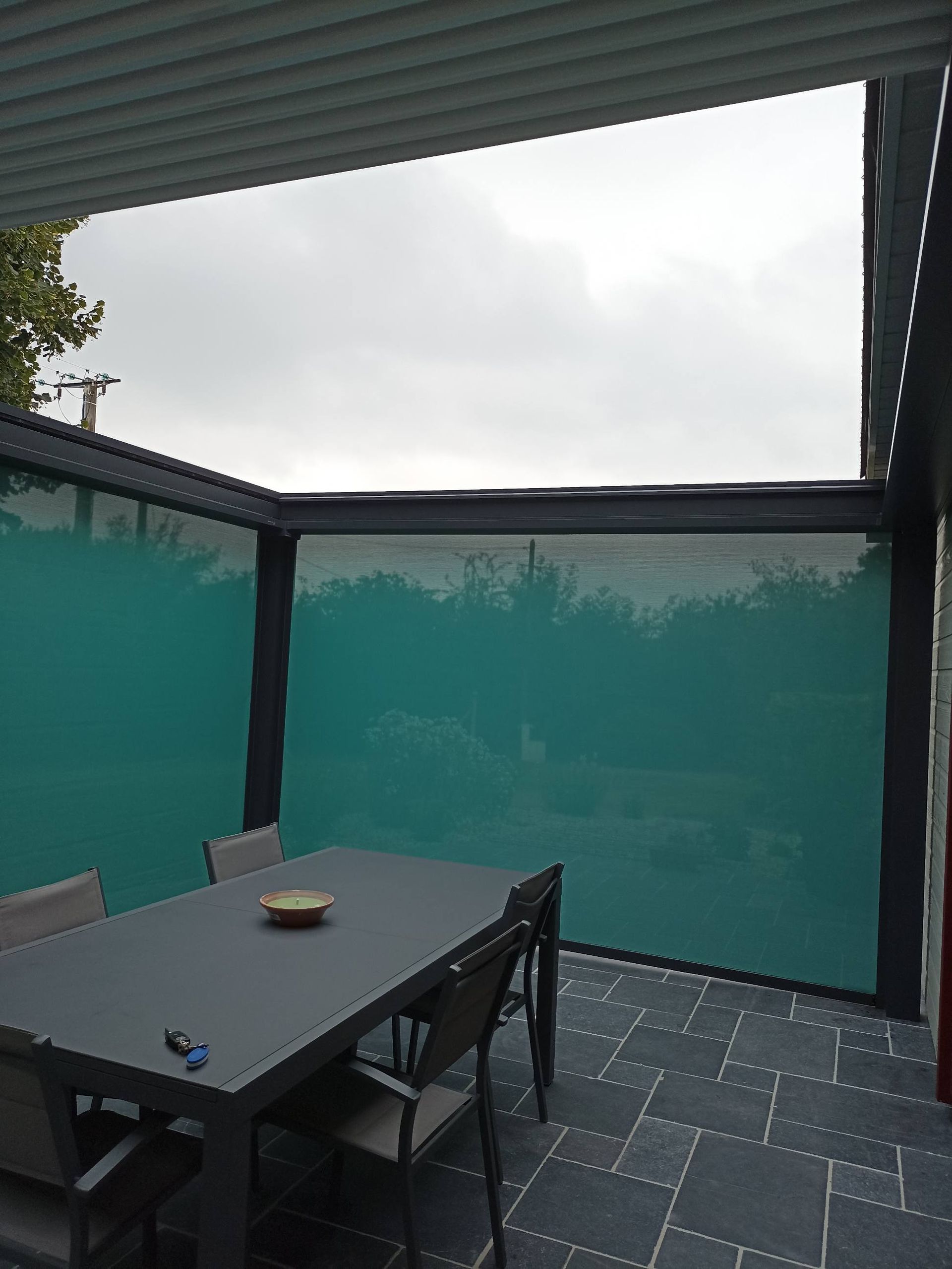 Terrasse extérieure avec table et chaises, écrans d'intimité bleu sarcelle et ciel nuageux.
