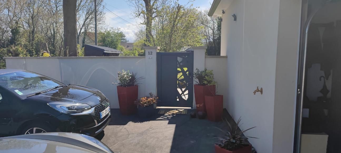 Une voiture noire garée devant une maison avec une entrée fermée et des pots de fleurs rouges.