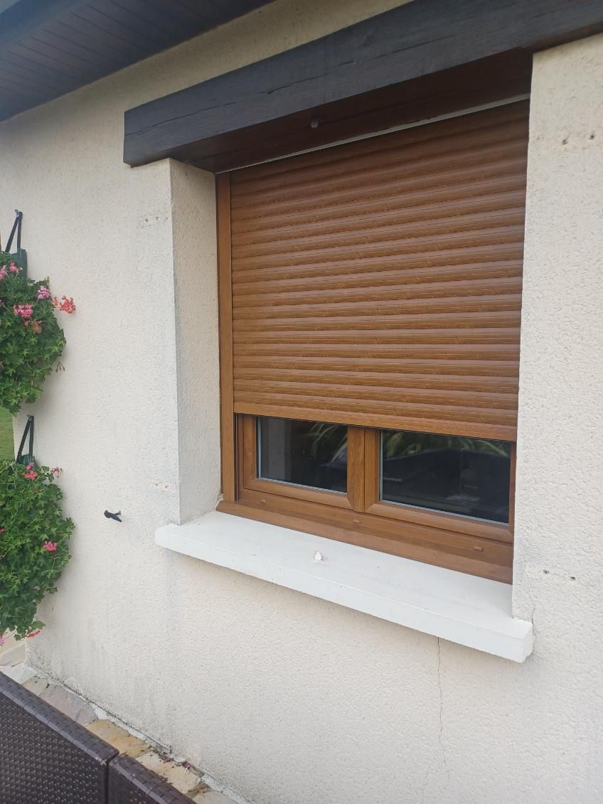 Fenêtre marron avec volet roulant marron fermé sur un extérieur de maison beige.