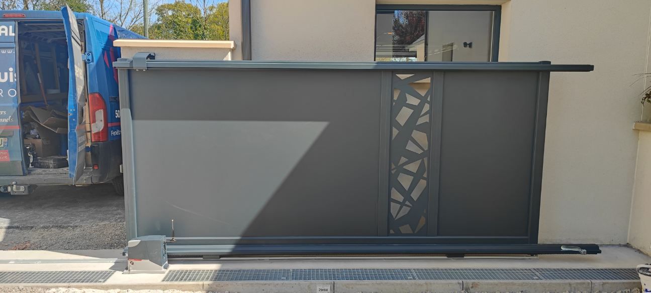 Un portail coulissant gris foncé avec un panneau découpé décoratif, placé devant une maison.