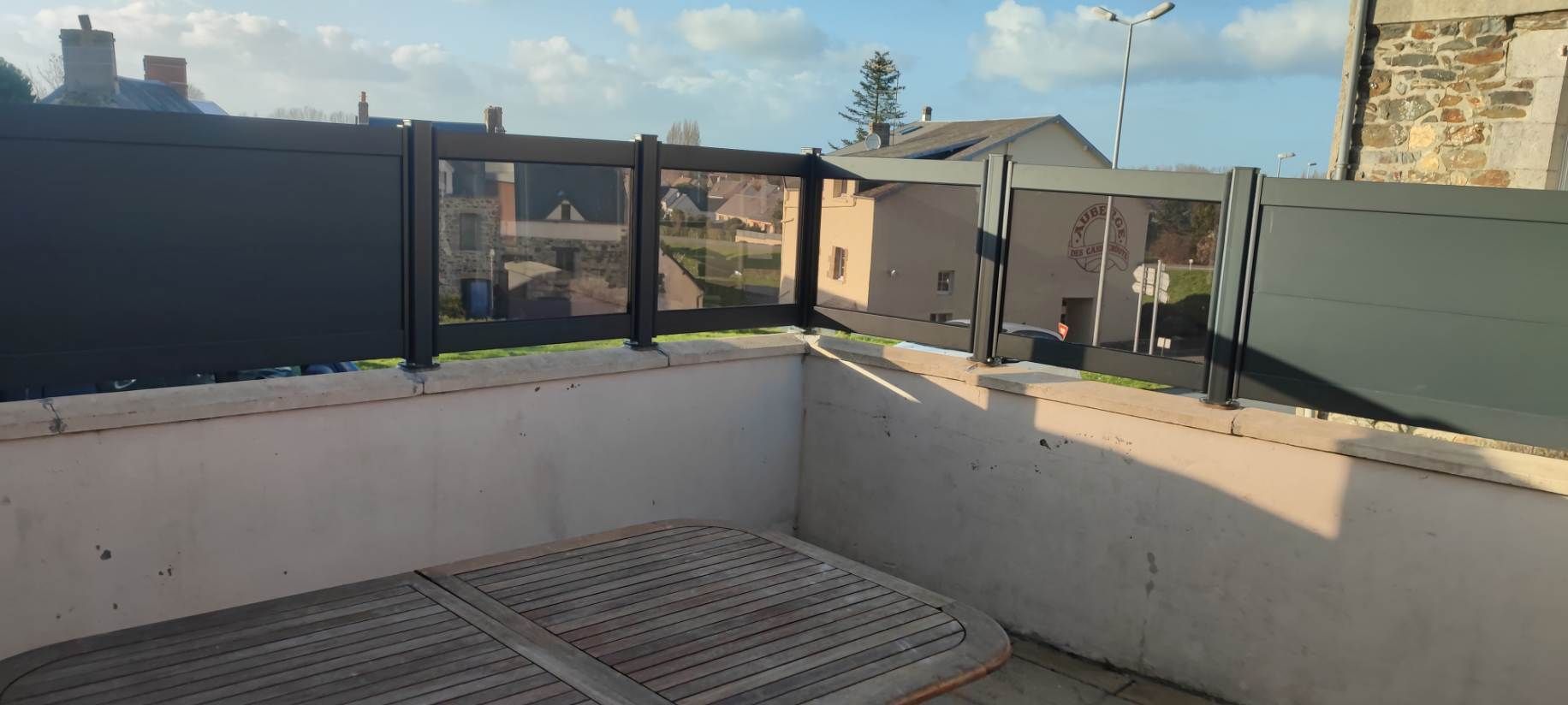 Une terrasse de couleur claire avec une clôture donnant sur un quartier résidentiel par une journée ensoleillée.