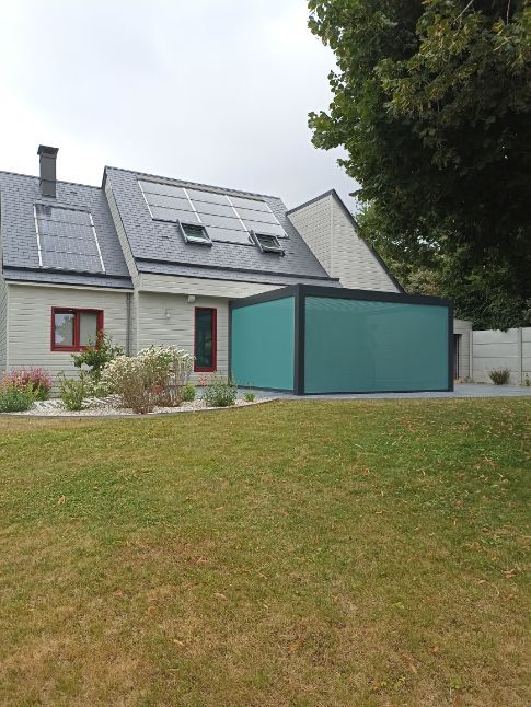 Une maison avec des panneaux solaires sur le toit et une structure extérieure bleu sarcelle. Une pelouse verte au premier plan.