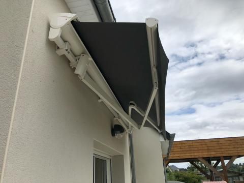 Auvent rétractable gris attaché à un bâtiment blanc sous un ciel nuageux.