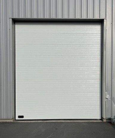 Porte de garage blanche fermée dans un bâtiment en métal gris.
