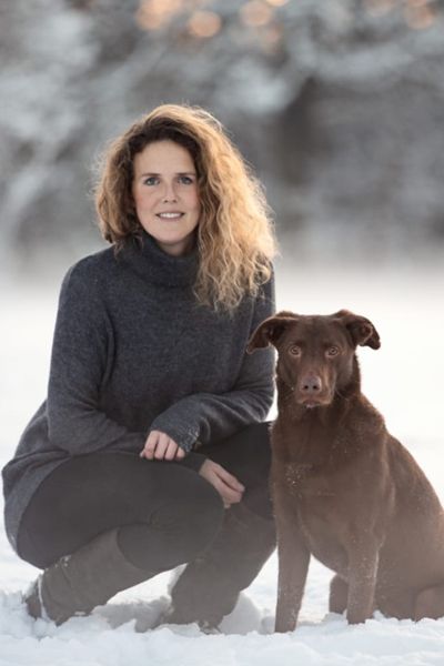 Eine Frau kniet neben einem braunen Hund im Schnee.