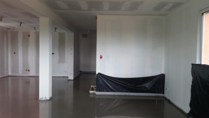 Pièce vide et inachevée avec des murs blancs, un sol brillant et des fenêtres laissant entrer la lumière du jour