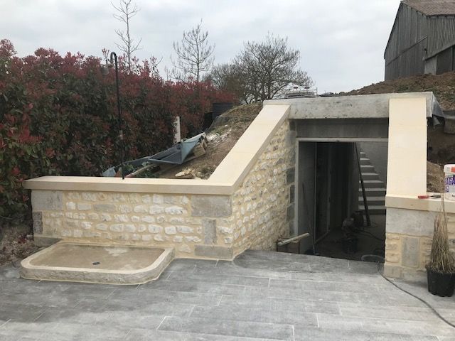 Rampe d'accès extérieure en pierre menant à une porte de sous-sol avec pavage en béton et mur de soutènement
