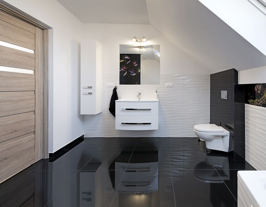 Salle de bains moderne avec sol noir brillant, meuble-lavabo blanc, lavabo, miroir, toilettes et paroi de douche carrelée.