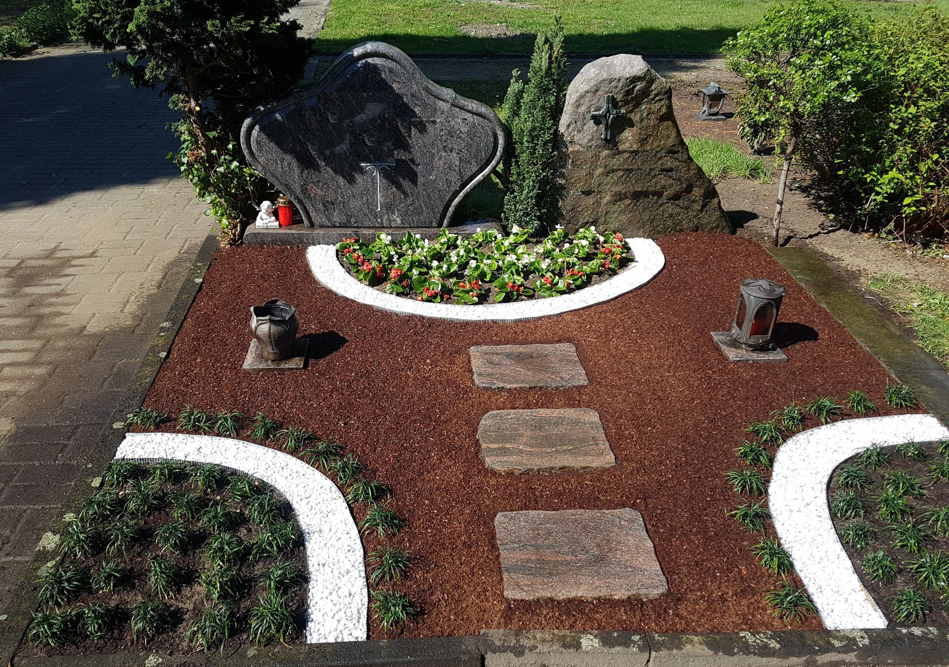 Grab mit schwarzem Stein, Steinweg, rotem Mulch, grünen Pflanzen und weißen Rändern.