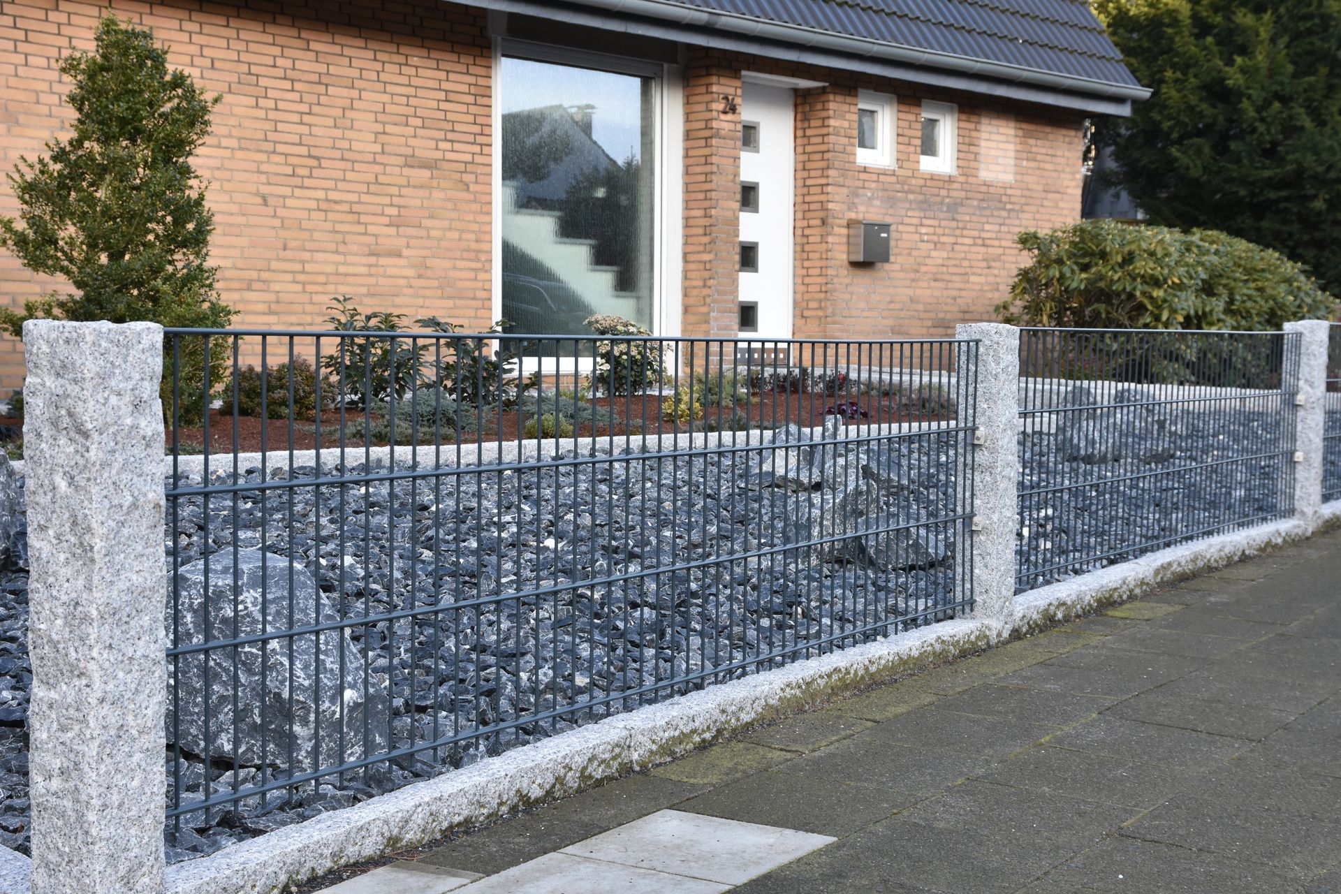 Stein- und Metallzaun, der ein Haus mit Ziegelfassade umgibt.