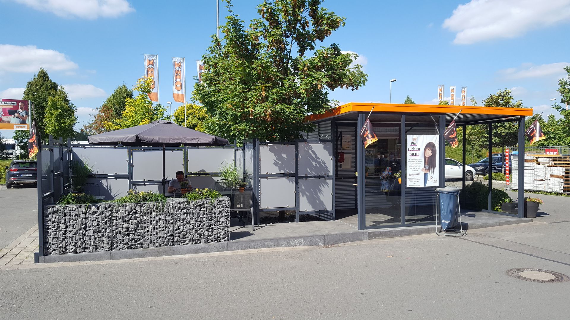 Sitzbereich im Freien mit grauen Wänden, einem Steinsockel und einem überdachten Unterstand mit Blumenbeeten.