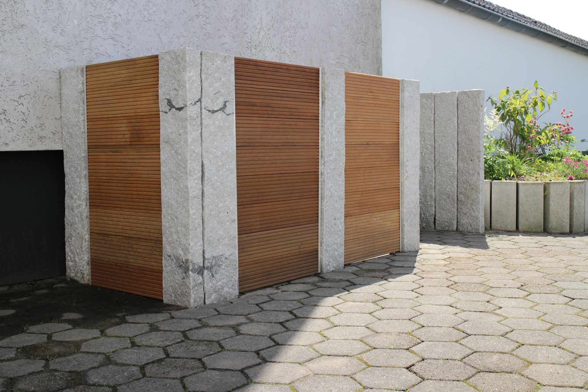 Von Steinsäulen eingerahmte Holzpaneele, zu denen ein gepflasterter Innenhof führt.