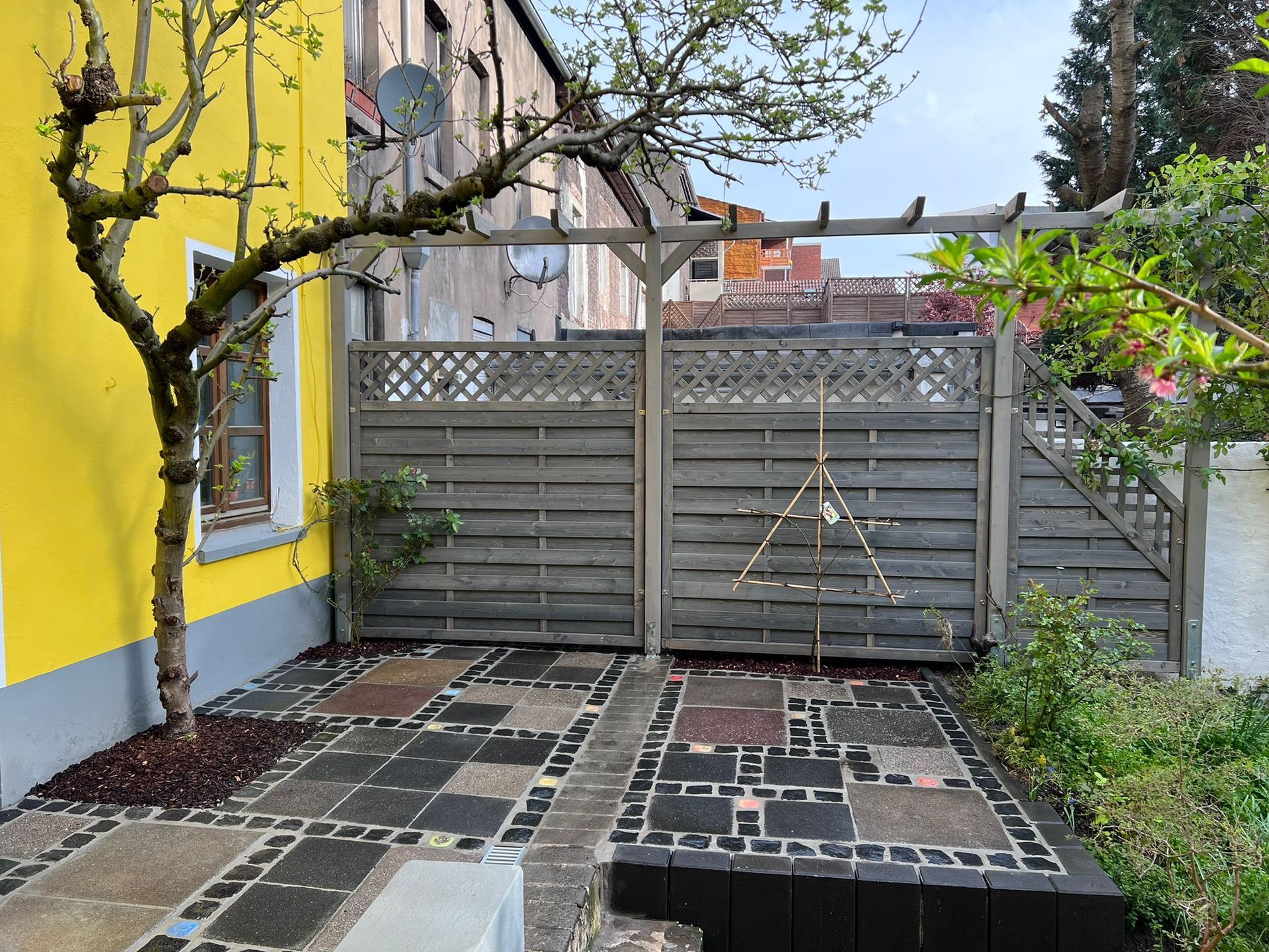 Hinterhofterrasse mit gelber Mauer, Holzzaun und Steinweg.