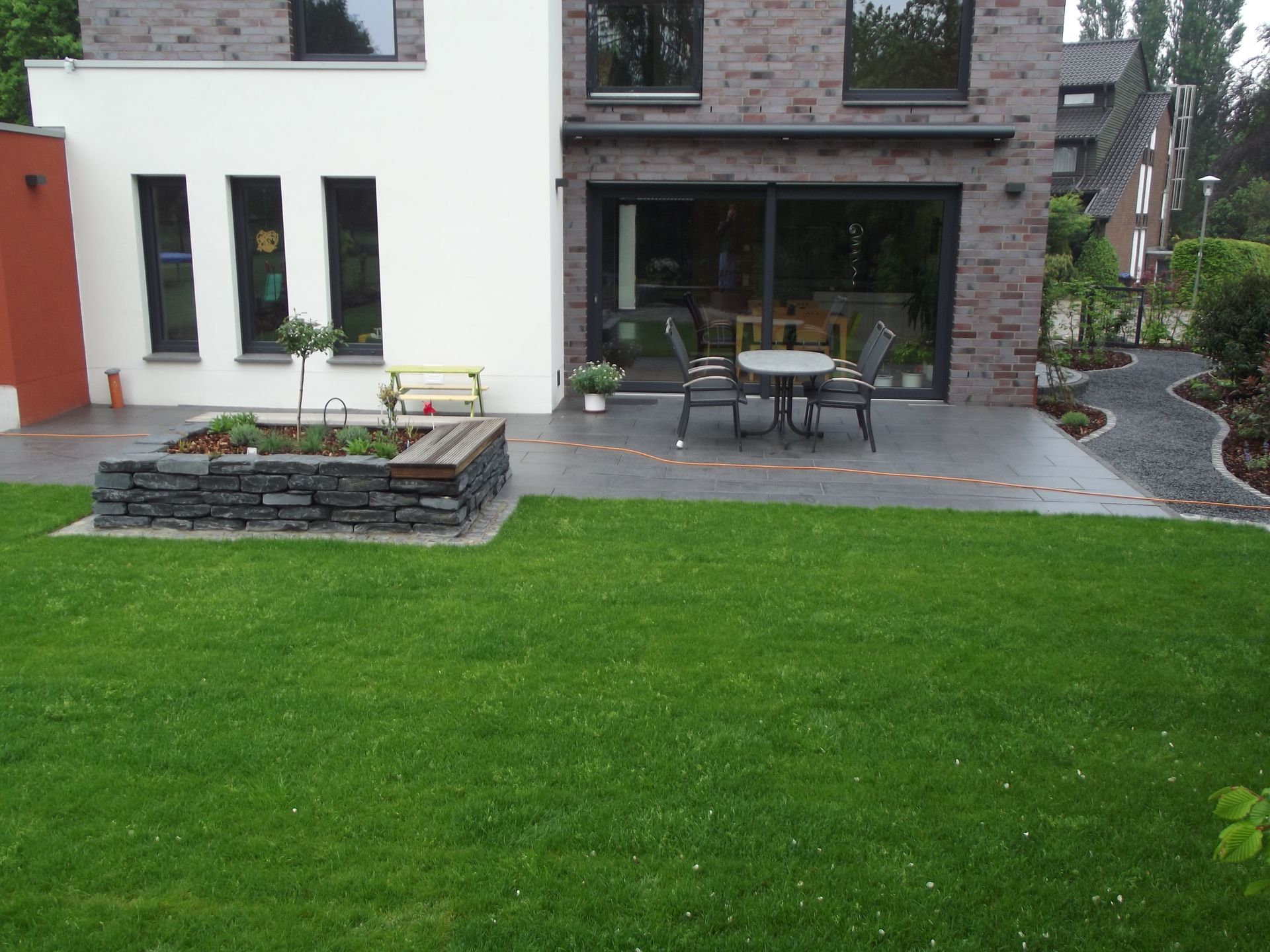 Hinterhofterrasse mit Tisch, Stühlen und Steingarten. Grüner Rasen, Backsteingebäude.