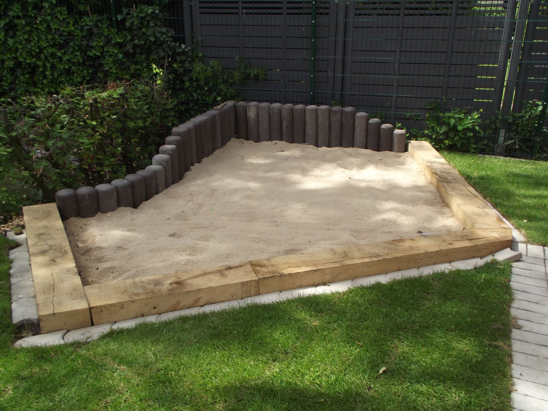 Sandkasten aus Holz und Betonblöcken in einem grünen Hof.