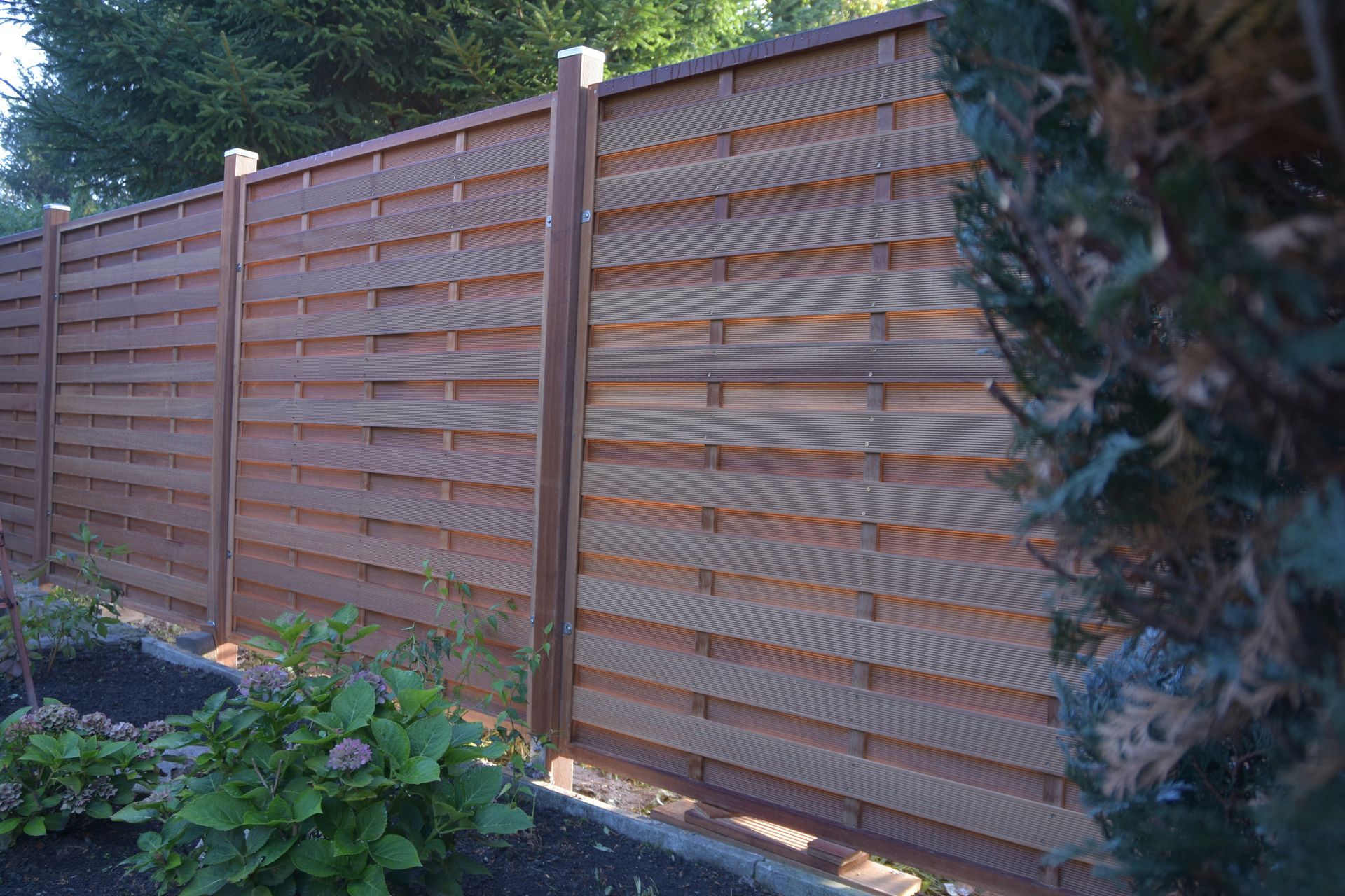 Brauner Holzzaun mit horizontalen Latten in einer Gartenumgebung.