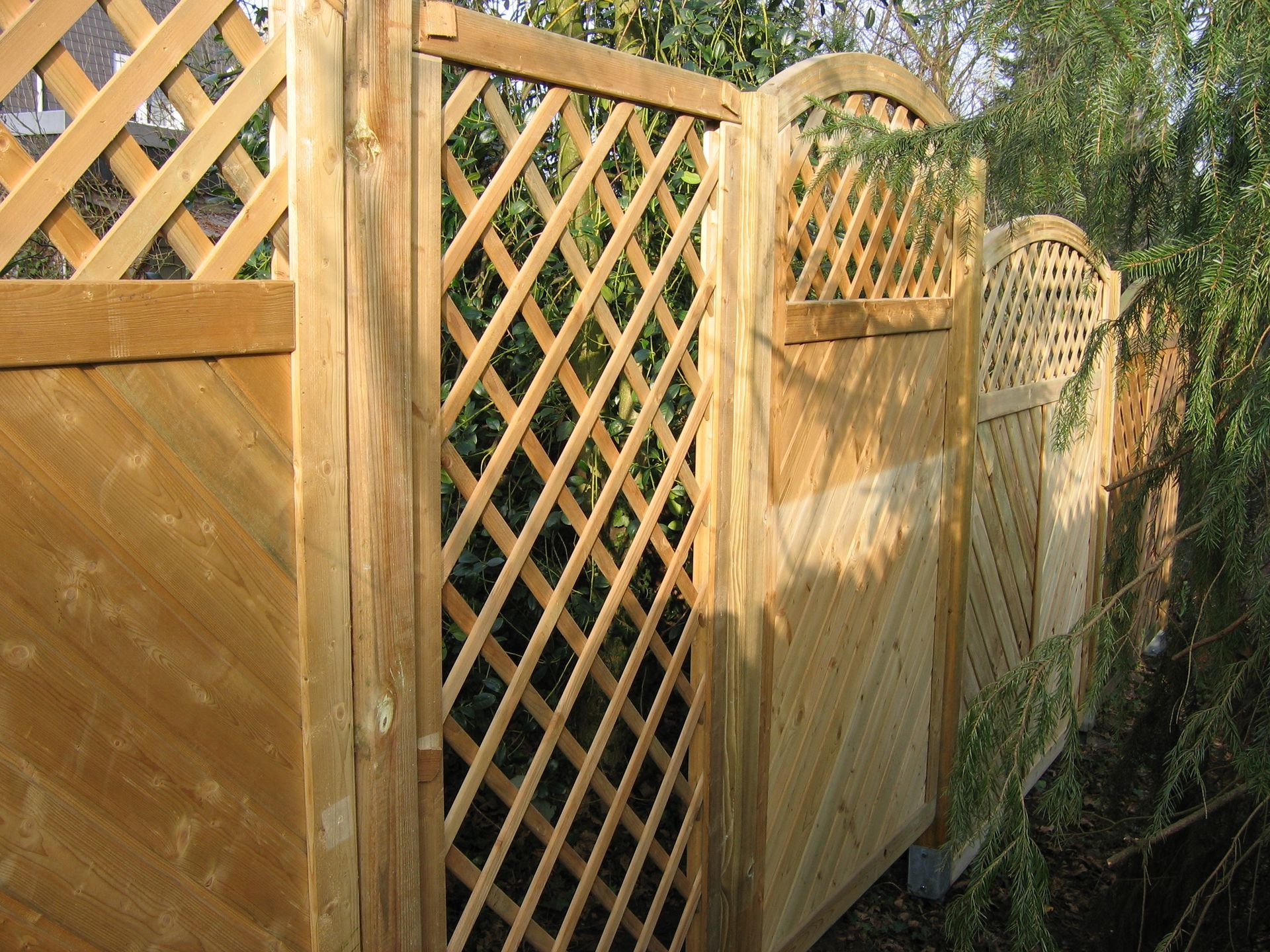 Gartenzaun aus Holz mit Gitterpaneelen und diagonalen Holzabschnitten.