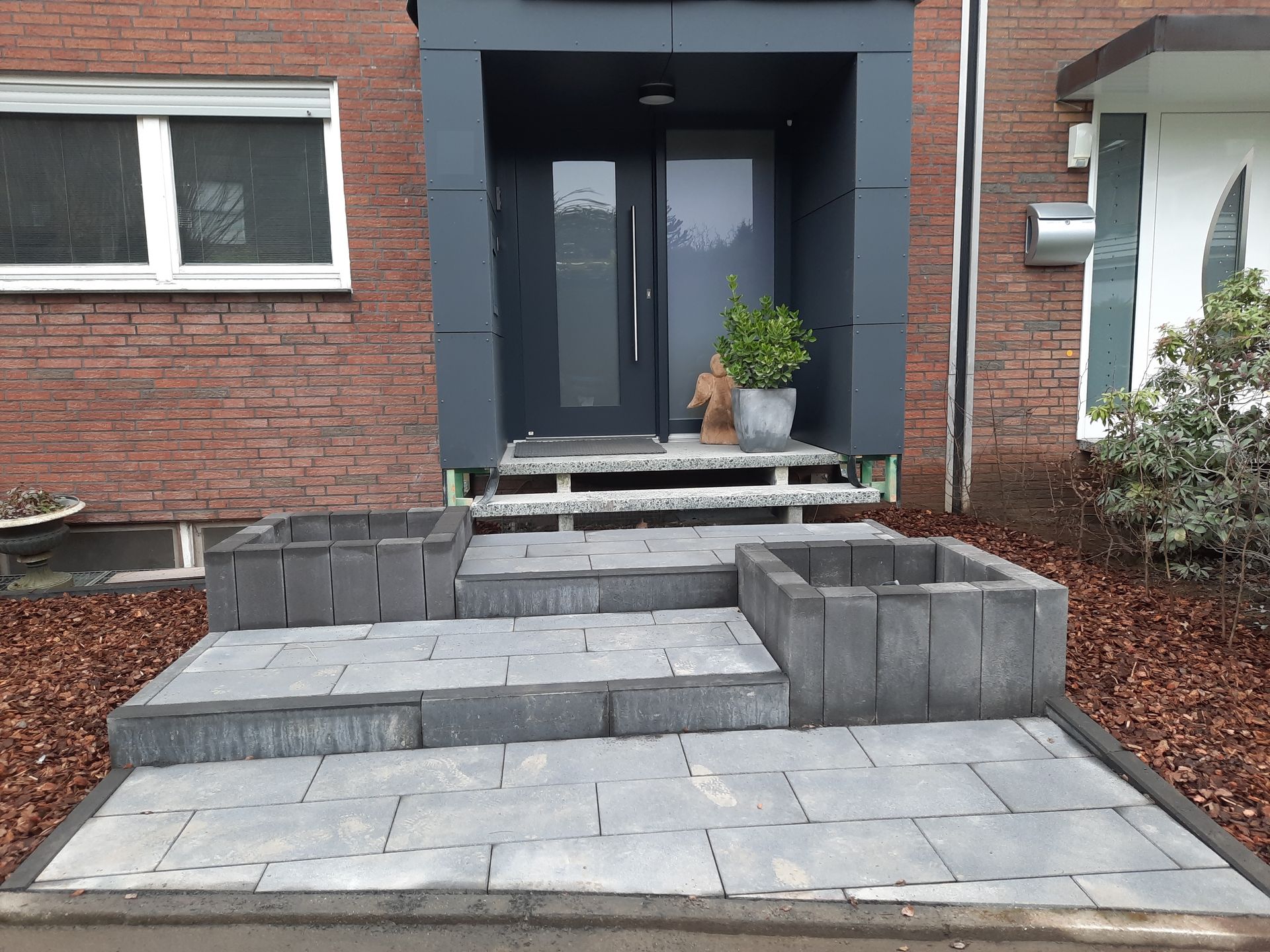 Hauseingang aus Backstein mit grauen Stufen, Pflanzgefäßen und Tür.