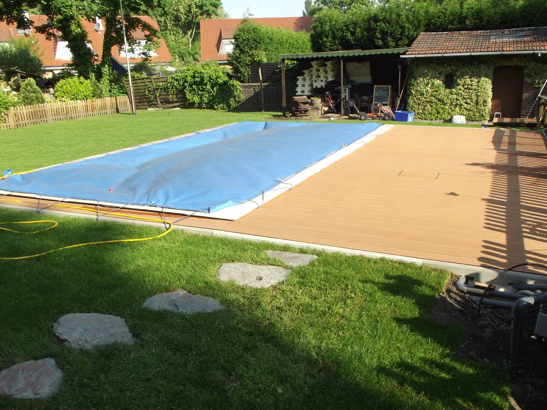 Hinterhof mit einem blau überdachten Pool, Gras, Steinweg und Schuppen an einem sonnigen Tag.