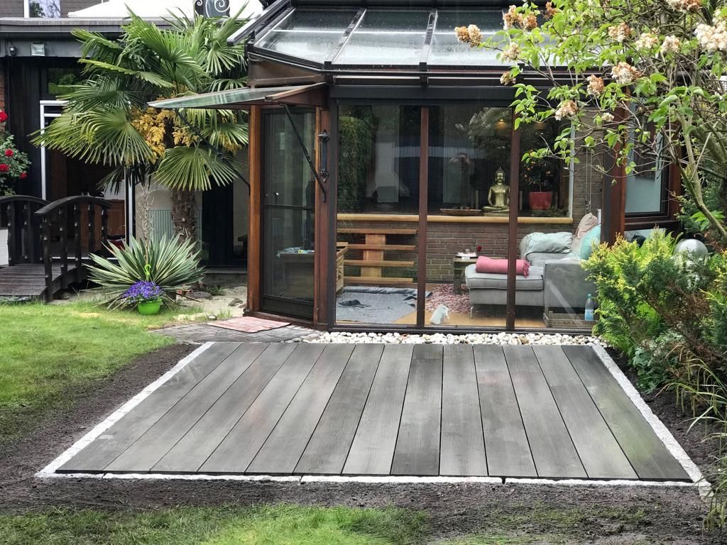 Holzterrasse mit Wintergarten mit Glaswänden; Gartenanlage im Freien.