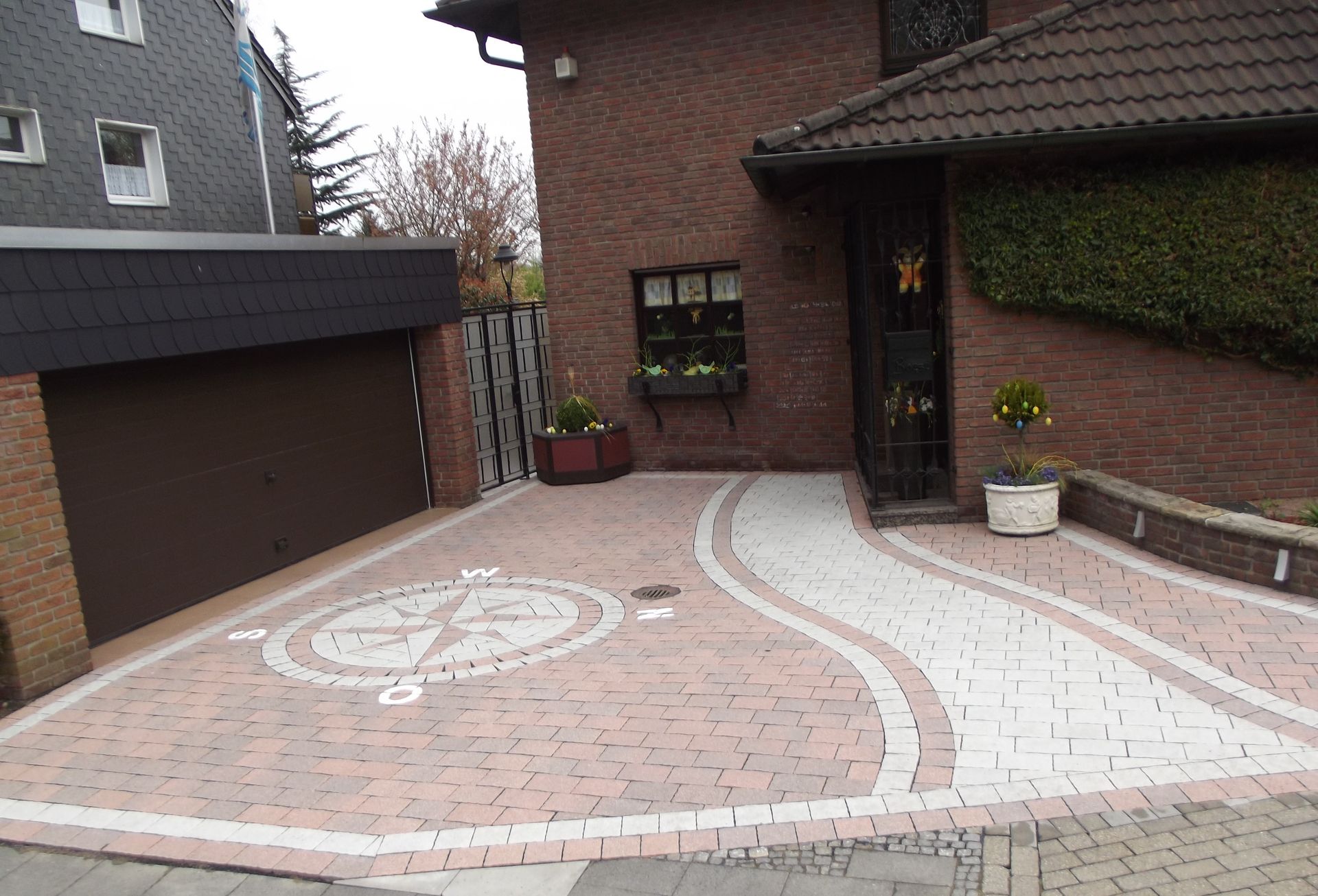 Backsteinhaus mit braunem Garagentor und gemusterter Auffahrt mit Windrosen-Design.