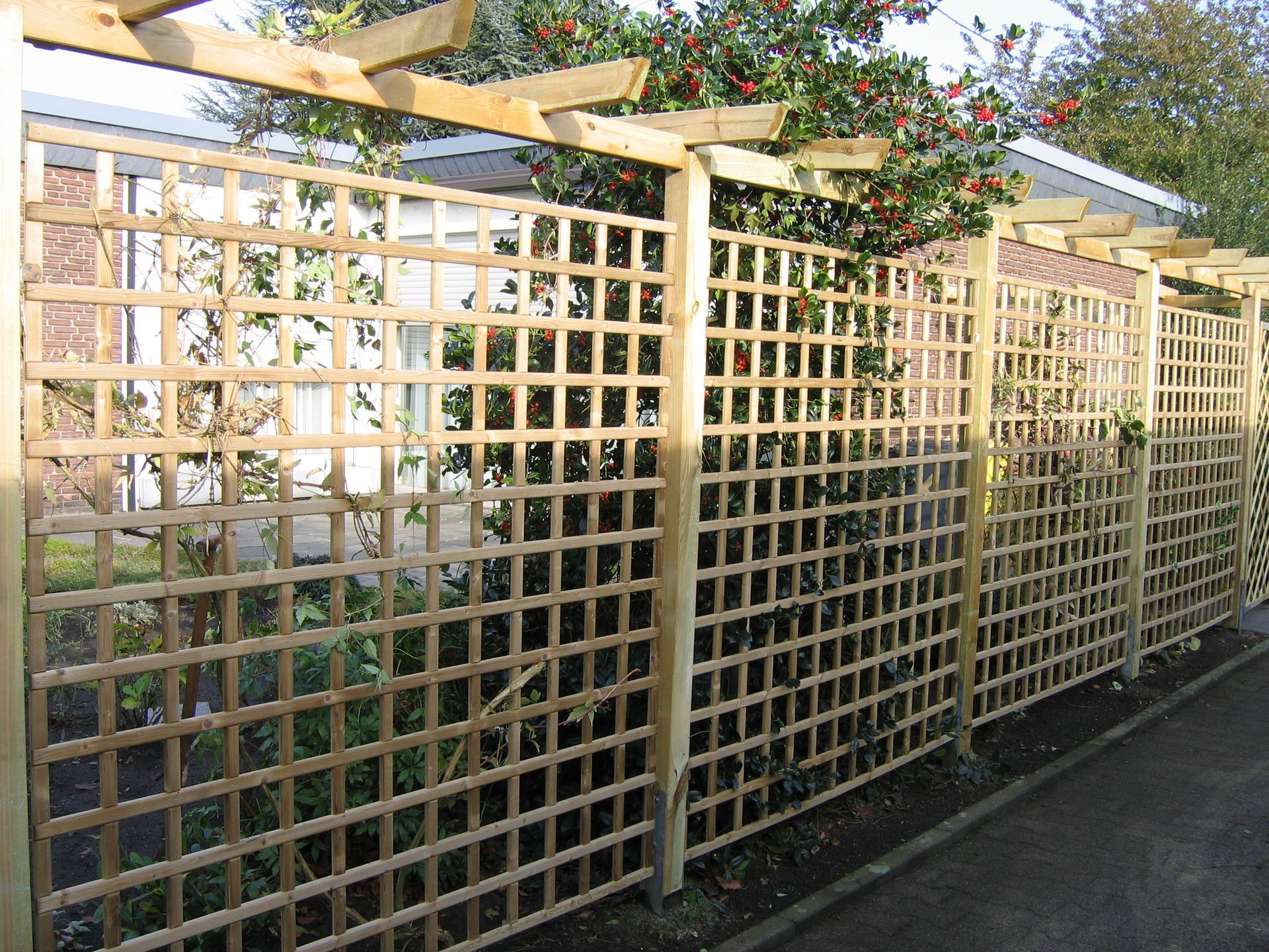 Holzgitterzaun mit quadratischem Gittermuster und oberem Pergolaabschnitt.