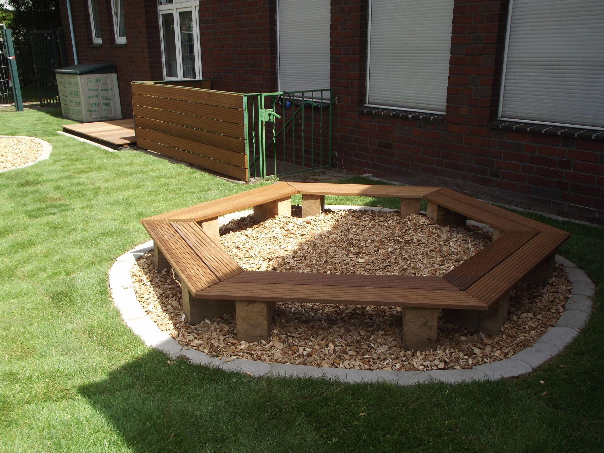 Holzbank umgibt eine Hackschnitzelgrube in einem Hof.