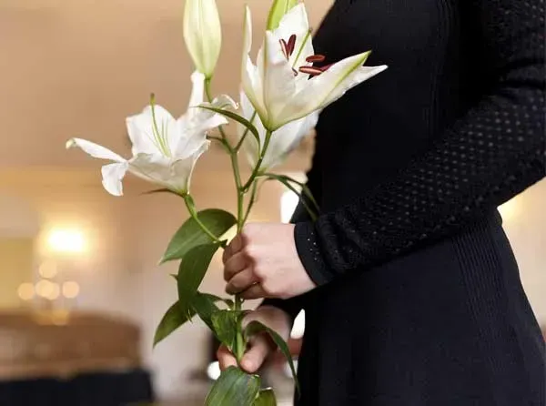 Una mujer con un vestido negro sostiene un jarrón de flores blancas.