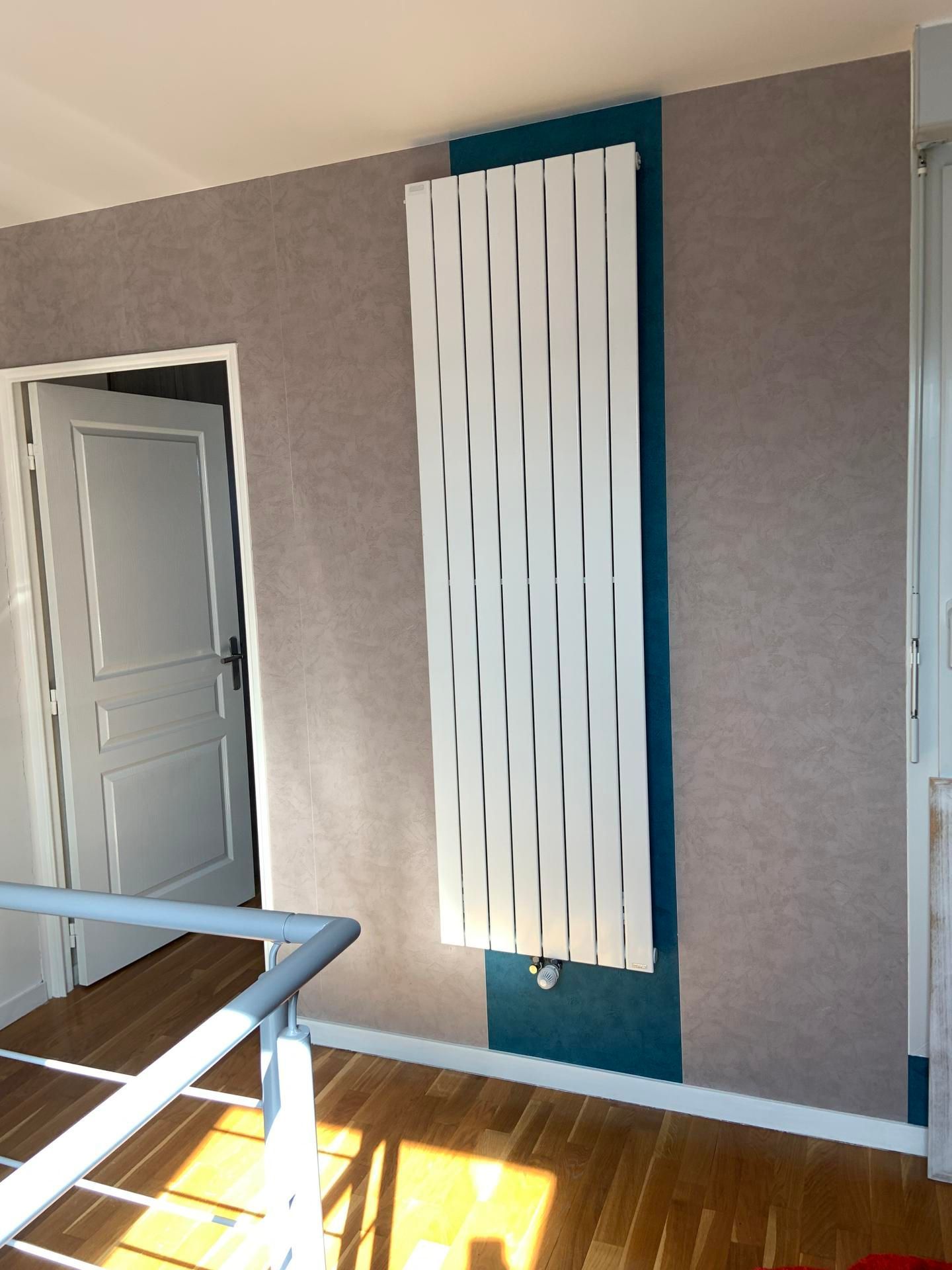 Radiateur blanc mural sur un mur d'accent turquoise dans une pièce ensoleillée avec parquet.