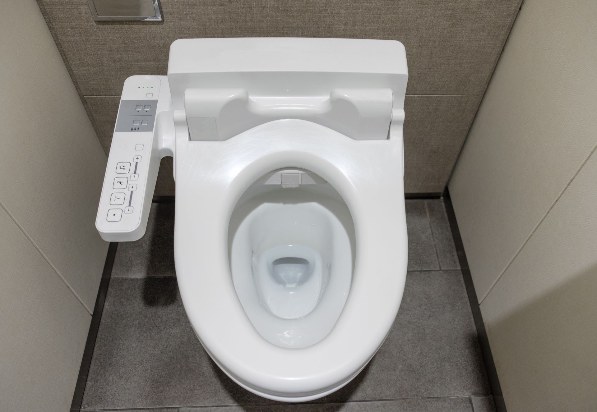 Vue de dessus de toilettes modernes blanches avec un panneau de commande latéral dans une cabine de toilettes.