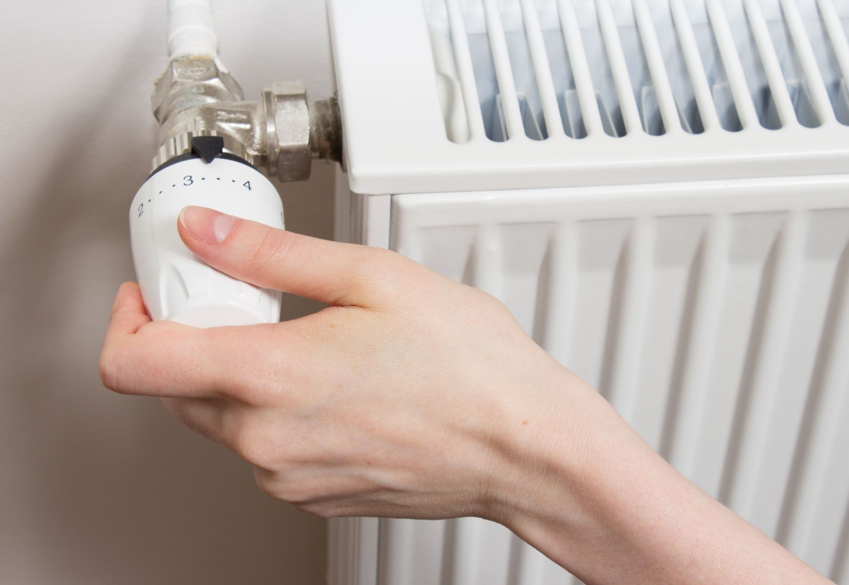 Actionnement manuel d'un robinet thermostatique sur un radiateur blanc