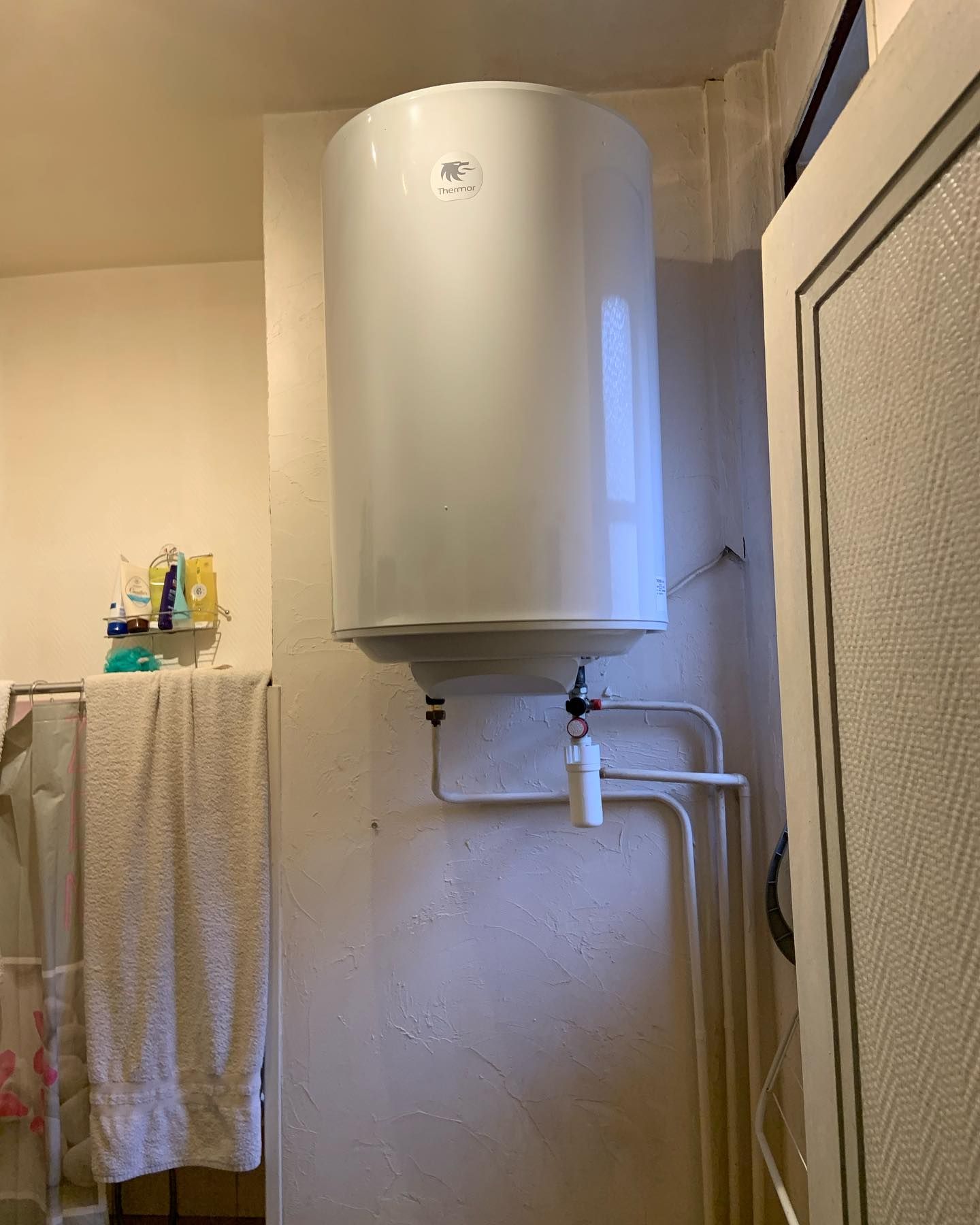 Chauffe-eau blanc installé au-dessus des tuyaux de la salle de bains et porte-serviettes à côté du rideau de douche.