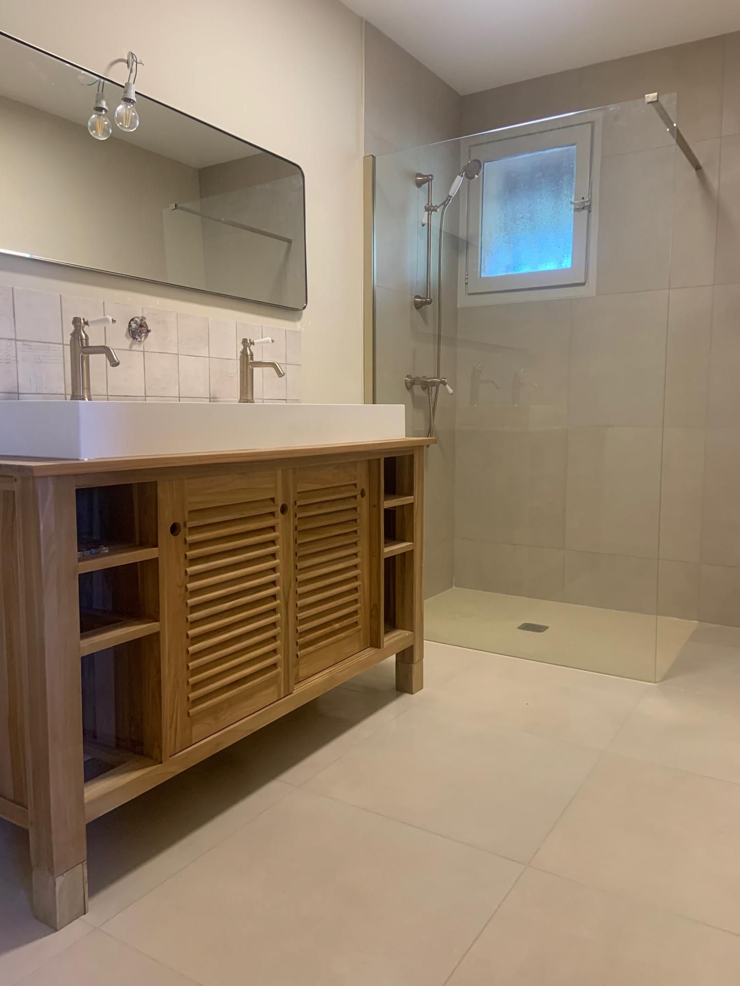 Salle de bains moderne avec meuble-lavabo en bois, grand miroir et douche vitrée avec fenêtre dépolie.
