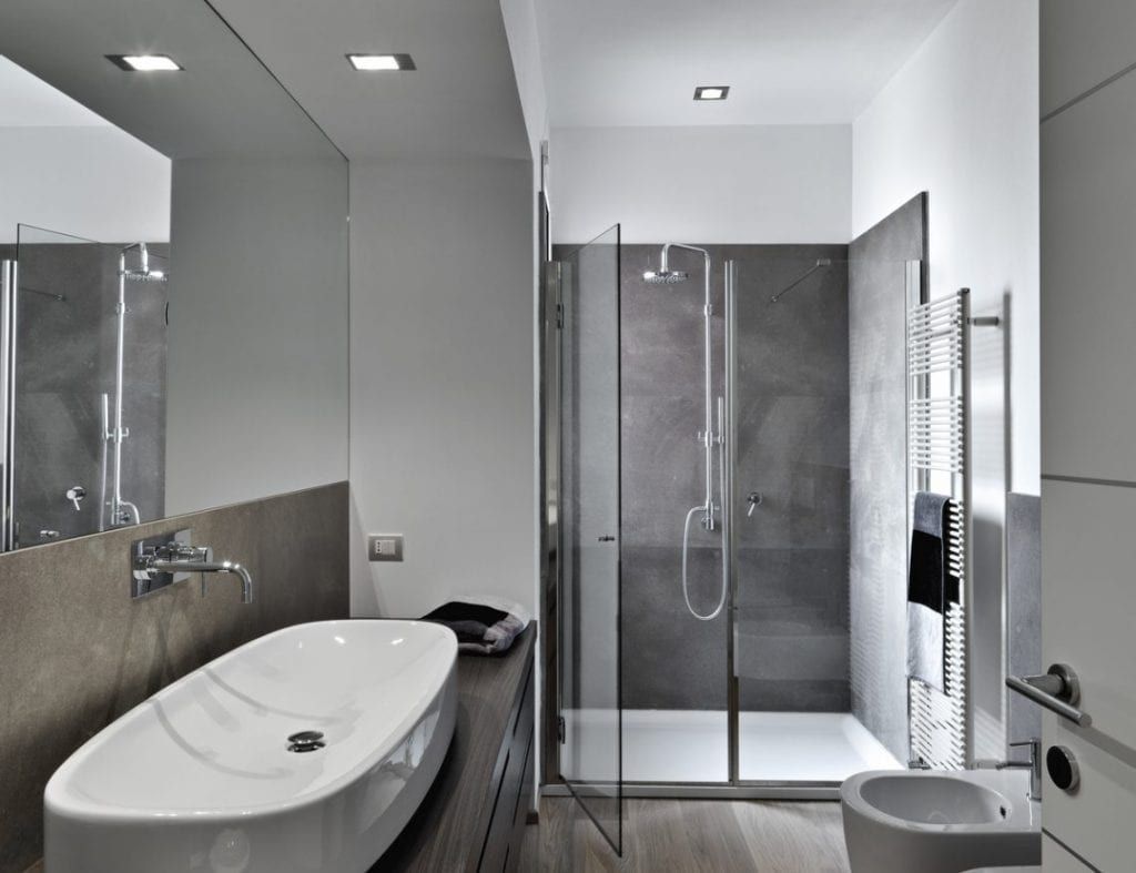 Salle de bains moderne avec baignoire, douche en verre, lavabo blanc et murs carrelés gris.