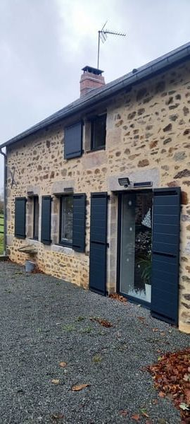 Maison en pierre avec volets bleus foncés vue de loin
