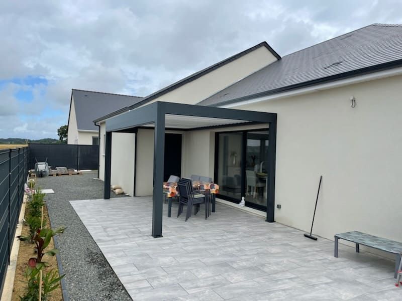 Pergolas noire sur terrasse grise avec maison à toit en ardoise