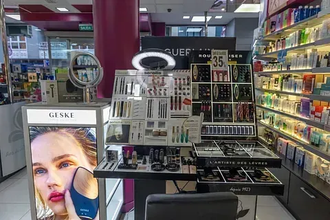 Un expositor de cosméticos en una tienda con un espejo y el rostro de una mujer en él.